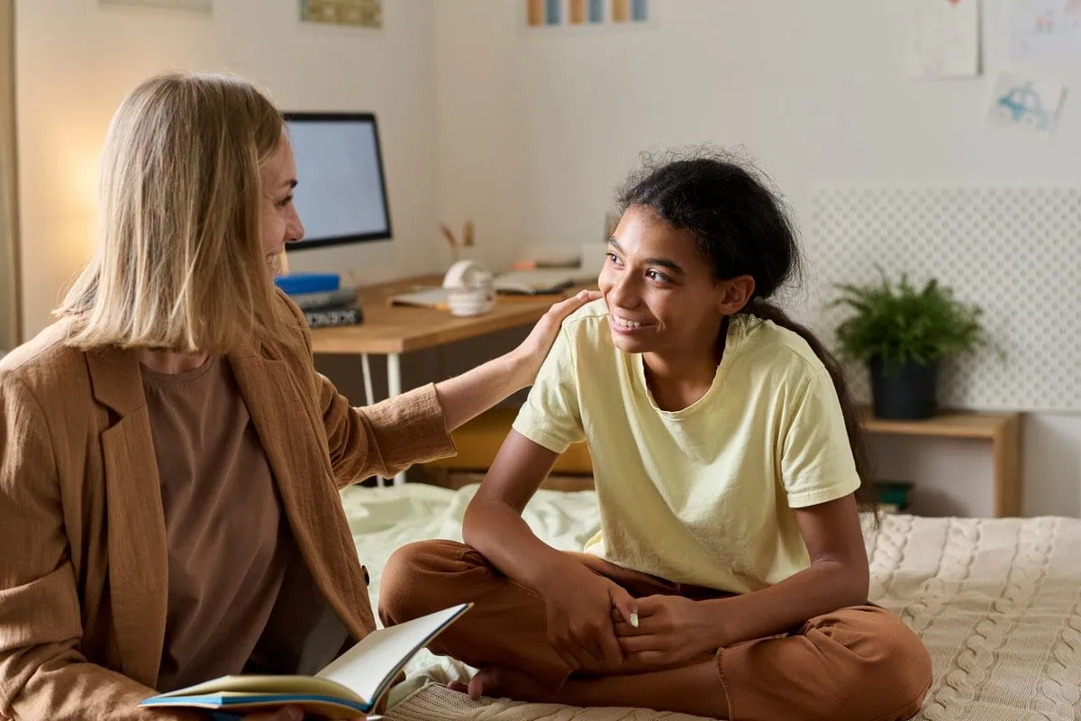 A teenage girl talking with a psychologist while sitting on a bed